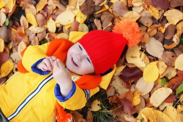 Kid in autumn park laying in leaves and smile