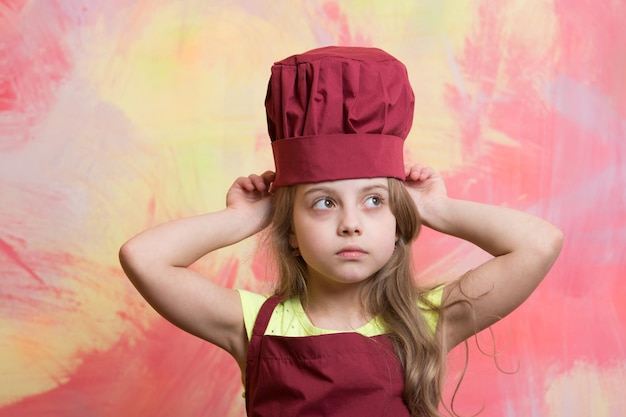 Photo kid or baby girl in cook or chef hat and apron on colorful abstract background kitchen and fashion