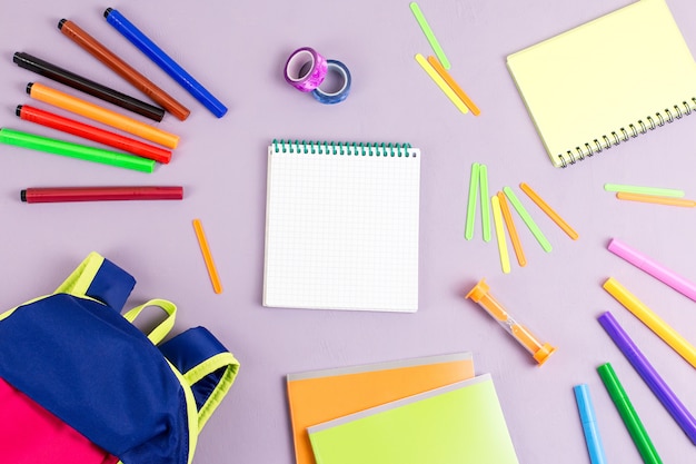 Kid backpack, notebooks, markers on wooden desktop, top view