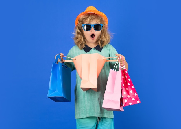 Kid boy in fashion clothes goes shopping. Kid with shopping packages. Shopper child with carrying shopping bags.