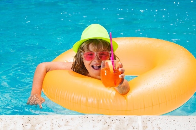 Kid boy hold healthy fruits and vegetables juice smoothie in summer pool Happy child enjoying organic drink Little child boy in swimming pool with inflatable toy ring Summer vacation