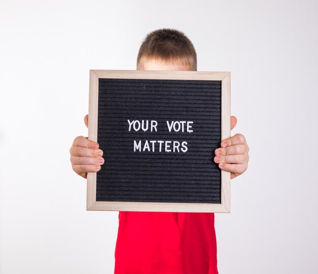 Kid boy holding letter board with text your vote matters on\
white background