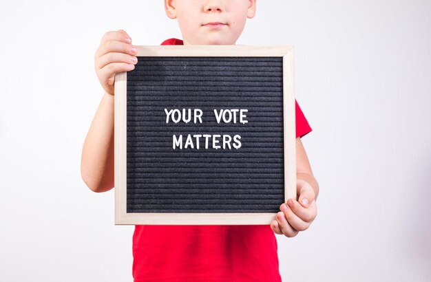 Photo kid boy holding letter board with text your vote matters on white background