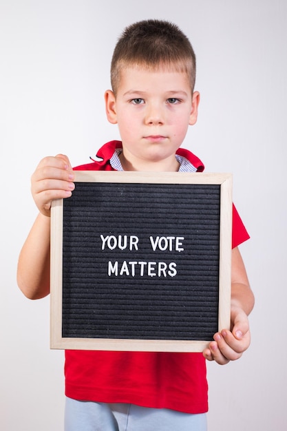 Photo kid boy holding letter board with text your vote matters on white background