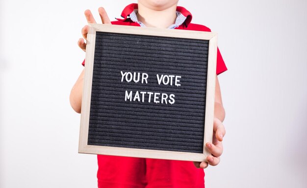 Foto kid boy holding letter board con testo your vote matters su sfondo bianco