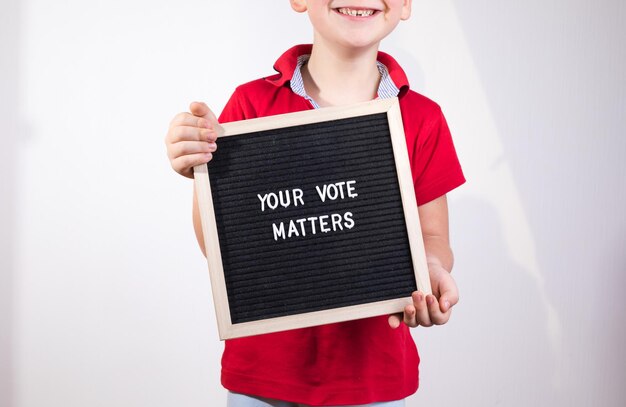 Photo kid boy holding letter board with text your vote matters on white background