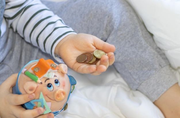 a kid boy is holding a piggy bank and some euro coins money concept saving and financial educati