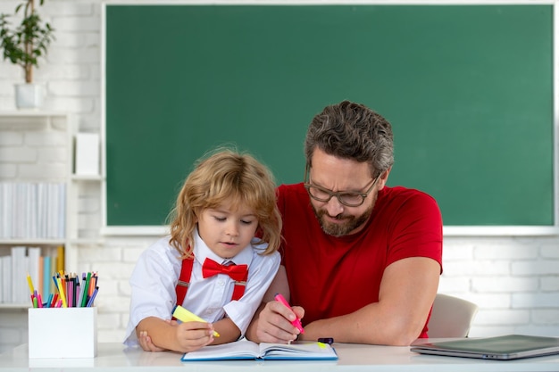 先生と一緒に学んでいる男の子おかしい男の子は黒板のクラスで父親と一緒に勉強します小学校の子供かわいい小学生の男の子