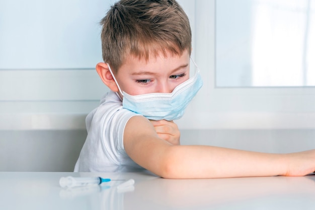 Kid boy lifts sleeve of Tshirt on arm to be vaccinated.