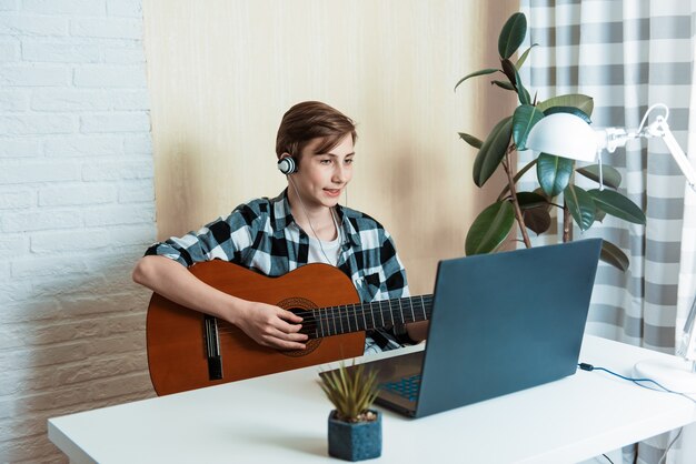 Premium Photo | Kid boy playing guitar and watching online lessons on  laptop while practicing at home. online training, online classes