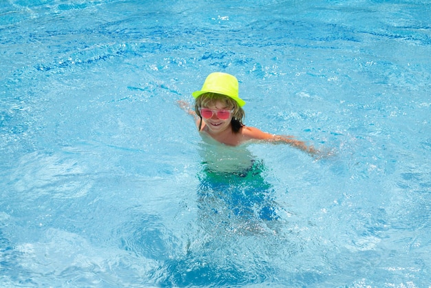 Kid boy playing in swimming pool Fashion summer kids in hat and pink sunglasses Child splashing in swimming pool