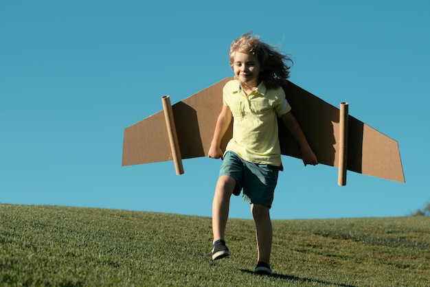 Kid boy playing with cardboard wings child in summer field kids travel and vacation concept imaginat