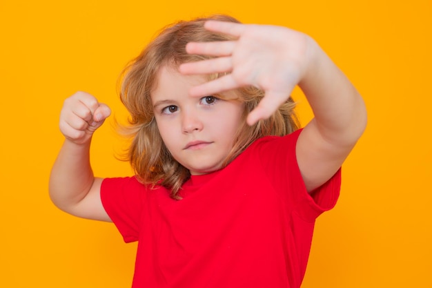 Photo kid boy in red tshirt making stop gesture on isolated studio background child with fist gesture figh