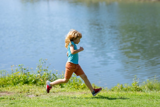 夏の公園で湖の近くの緑の芝生の上を走っている子供の少年夏 pa で実行されているスポーティな子供少年ランナー