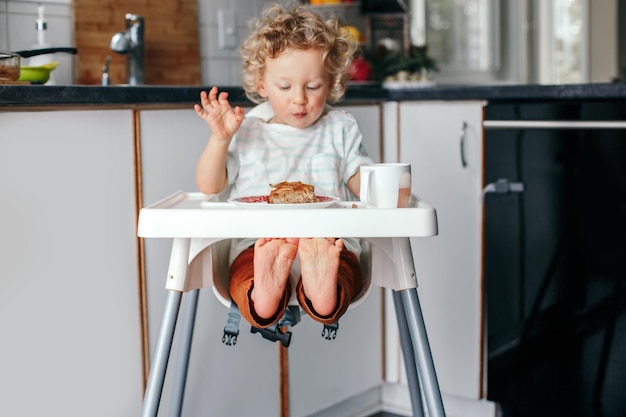 kid boy sitting in high chair eating homemade apple pie and drinking juice toddler enjoying food