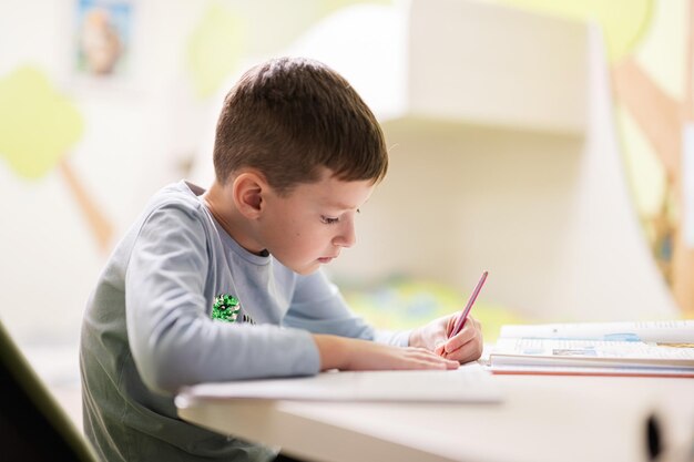 Kid boy studying at home and doing school homework distance learning education sitting at table