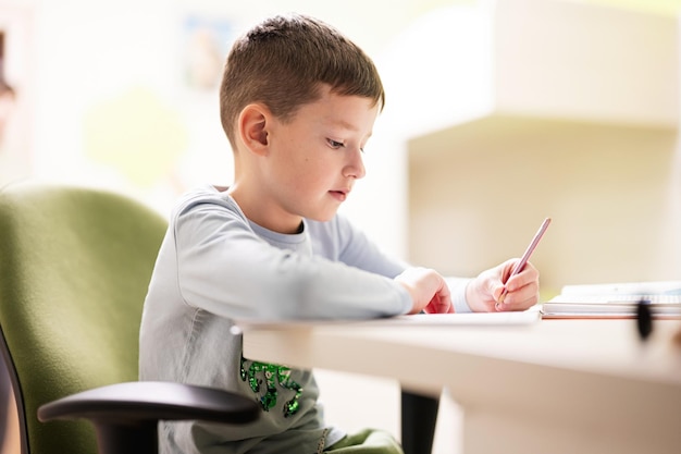 Мальчик учится дома и делает домашнее задание в школе, дистанционное обучение, сидя за столом