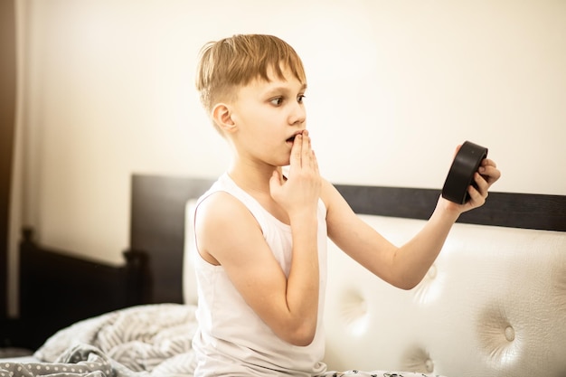 Kid boy teenager waking up shocked looking alarm clock in morning