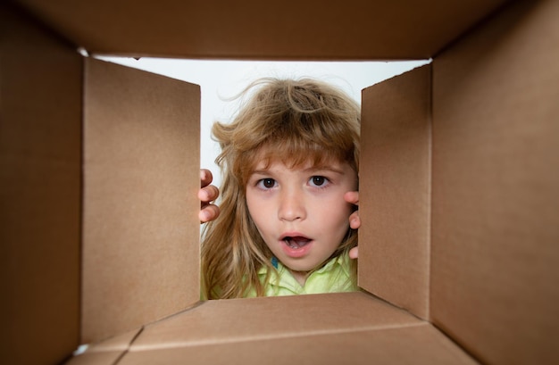Фото Мальчик распаковывает и открывает картонную коробку, глядя внутрь с удивленным лицом. мальчик открывает пакет.