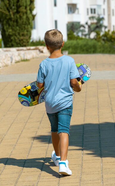 Kid boy walking with a skateboard in hands in park