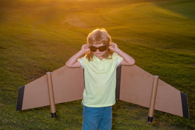 Kid boy with pilot glasses flying in plane made craft of cardboard wings dream imagination childhood...