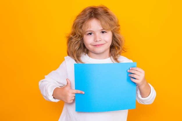 Kid boy with sheet of paper isolated on yellow background portrait of a kid holding a blank placard