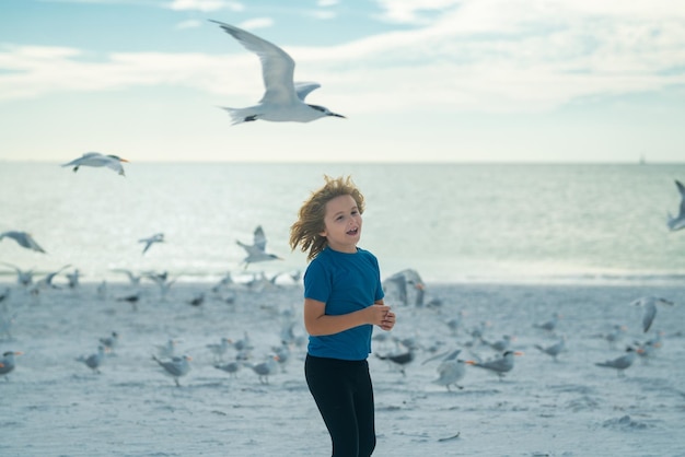 Kid chasing birds near beach on summer day child and seagull on the sea excited boy running on the b