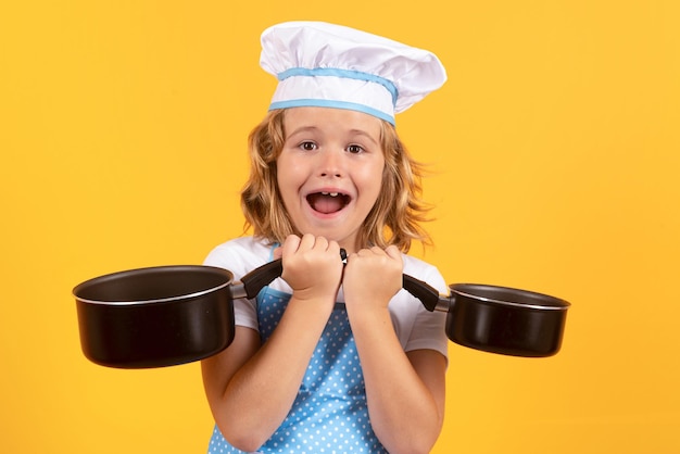 Kid chef cook with cooking pot stockpot Child chef cook prepares food on isolated studio background Kids cooking Teen boy with apron and chef hat preparing a healthy meal