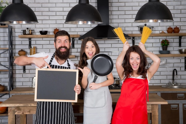 Kid chef with her parents Mother and father teaching daughter how to cook happy family day mutual assistance and support friendly family in kitchen cooking healthy food at home copy space