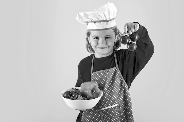 Kid cook hold tomato Portrait of little child in uniform of cook Chef boy isolated on studio background Cute child to be a chef Child dressed as a chef hat