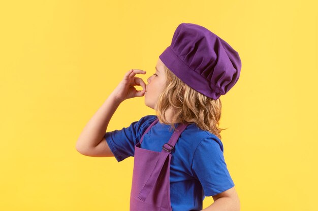 Kid in cooker uniform and chef hat preparing food on studio color background Cooking culinary and kids food concept