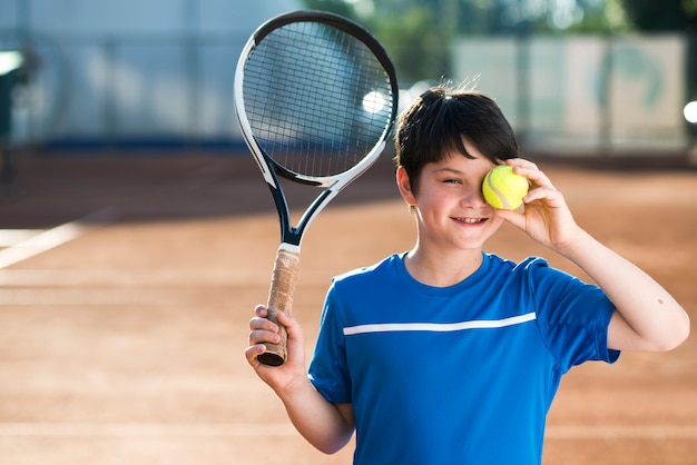 Kid che copre il suo occhio con la pallina da tennis