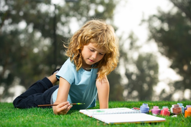 Kid draws in park laying in grass having fun on nature background children artist paints creativity