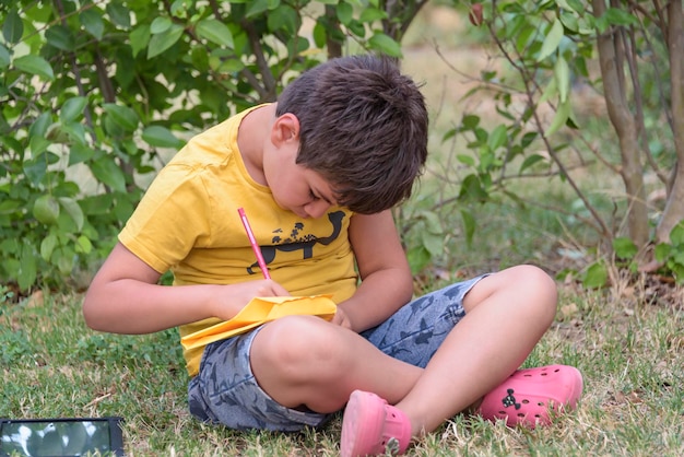 Малыш рисует в парке, лежа на траве, весело проводя время на фоне природы