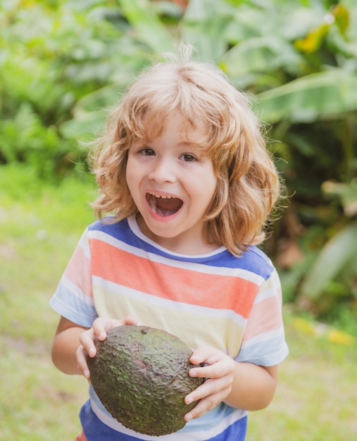 자연 배경에서 아보카도를 먹고 즐기는 아이. 어린이 개념을 위한 건강 식품.