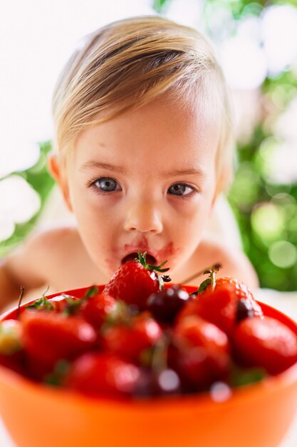 Kid eating strawberries from a bowl of fruit