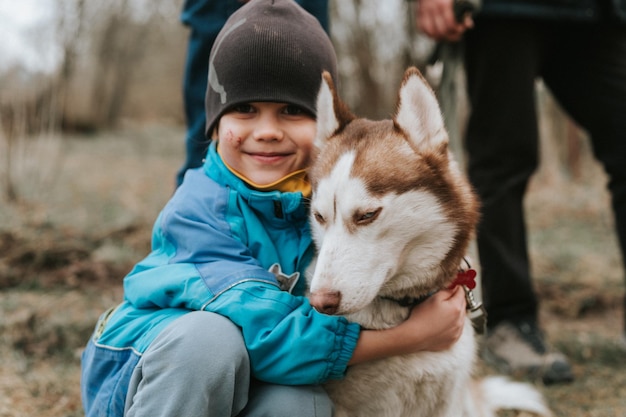 Kid en zijn vriend husky siberische hond portret klein kind jongen knuffelen schattig wit bruin zoogdier dier huisdier van een jaar oud met blauwe ogen in de herfst rustiek en platteland natuur bos