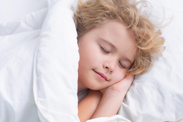 달콤한 꿈을 즐기는 아이 침대에서 자고 있는 어린 소년 귀여운 아이가 담요 아래 침대에서 혼자 잘 자고 있습니다.