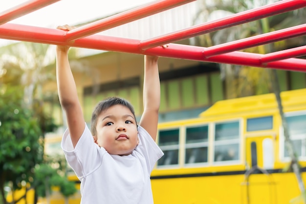 Kid exercise for health and sport concept. Happy Asian student child boy playing and hanging from a steel bar at the playground.