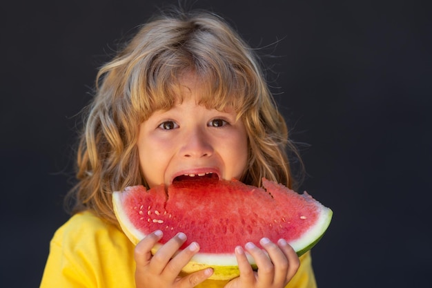 子供の顔とスイカをクローズ アップ興奮した子供がスイカを食べる子供は灰色の背中にスイカを摘んでいます