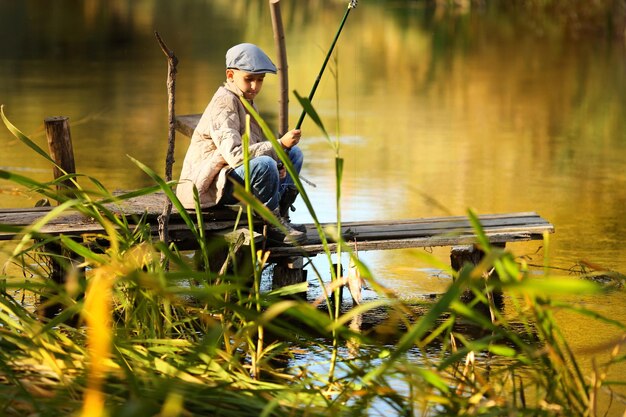 Малыш ловит рыбу в реке, сидя на деревянном понтоне