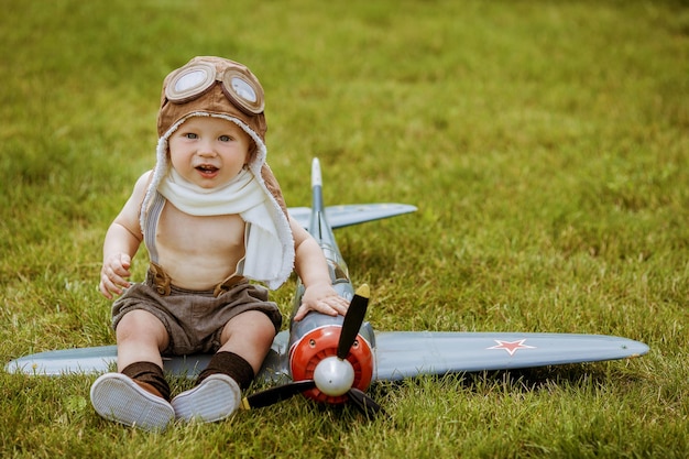 パイロットの形をした子供が芝生の上で飛行機で遊ぶ小さな男の子は飛ぶことを夢見ています