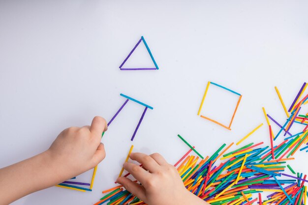 Kid geometrische vormen maken met kleurrijke stokken op witte achtergrond