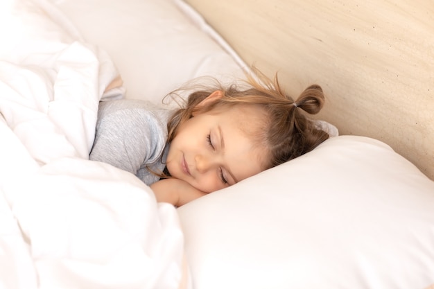 Kid gesloten ogen liggend in bed slapen op kussen en onder witte katoenen deken goedenacht zoete dromen