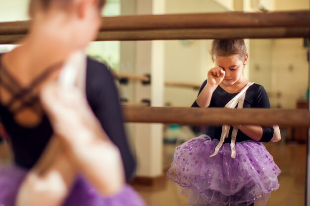 ポアントシューズを持ち、ハードトレーニングの後に涙を染めるダンスクラスの子供女の子。子供とスポーツのコンセプト