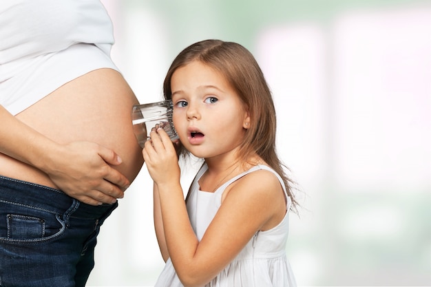 Kid girl listening with can pregnant mother's stomach