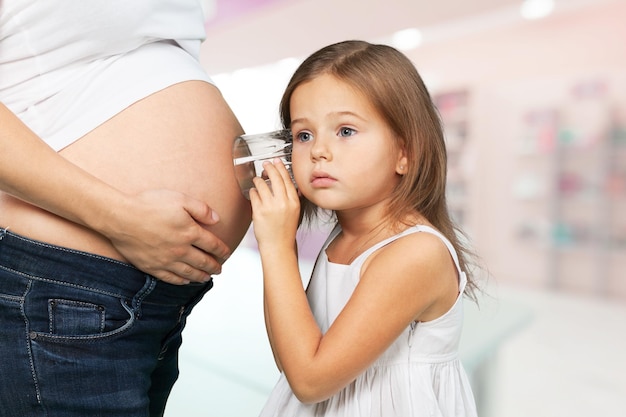 Kid girl listening with can pregnant mother's stomach