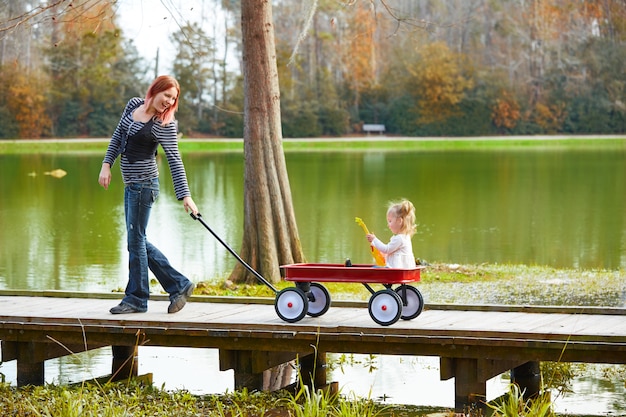 Kid girl and mother walking in lake with pull cart