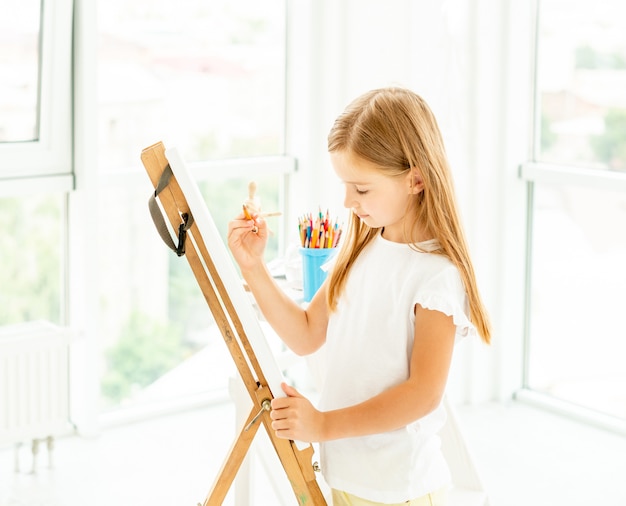 Photo kid girl painting different pictures on easel