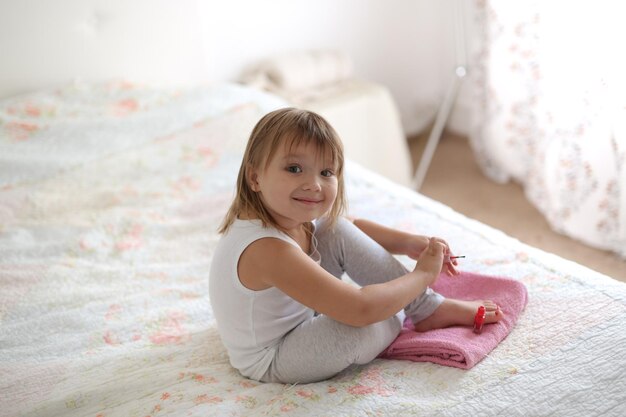 Kid girl paints nails on the bed real light interior and lifestyle concept childhood